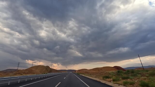 Car traveling along highway, wide view, through open countryside in Turkey beneath storm clouds, showing long-distance mobility, changing weather, road infrastructure, self-drive tourism