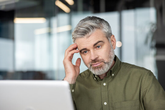 Focused mature businessman with a headache touching his temple, thinking deeply and concentrating on work, experiencing stress and burnout in an office environment
