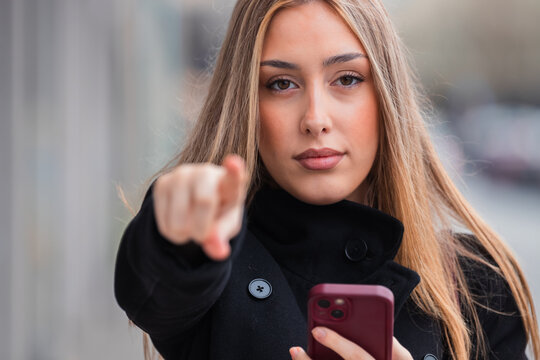 young woman pointing at camera with mobile phone