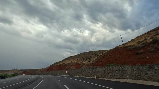 Car traveling on a curving highway in wide view beneath heavy storm clouds in Turkey, showing changing road conditions, regional transport, route planning, travel safety, and long-distance mobility