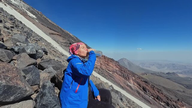Female tourist drinks water in side view on Mount Ararat during an acclimatization hike, highlighting high altitude hydration, mountain trekking, expedition training, endurance, and adventure travel