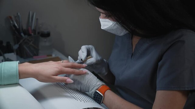 Applying glitter color gel coating to extended nail by nail technician during professional salon manicure procedure