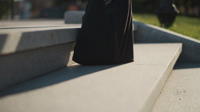 Close up of black bag being placed on concrete steps with sunlight casting shadows. hand places eco friendly mesh net containing oranges next to dark fabric item emphasizing sustainable
