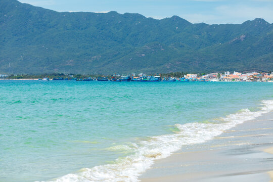 Scenic beach view in Vietnam with turquoise water, gentle waves, and distant mountains under a clear sky, featuring a coastal town in the background