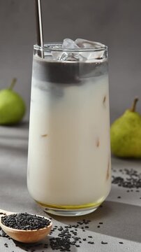 Metal straw slowly stirs black sesame paste into iced oat milk and pear syrup, creating marbled layers in autumn latte drink.