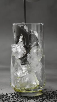 Black sesame paste pours over ice in clear glass, coating cubes with dark creamy texture during layered drink preparation.