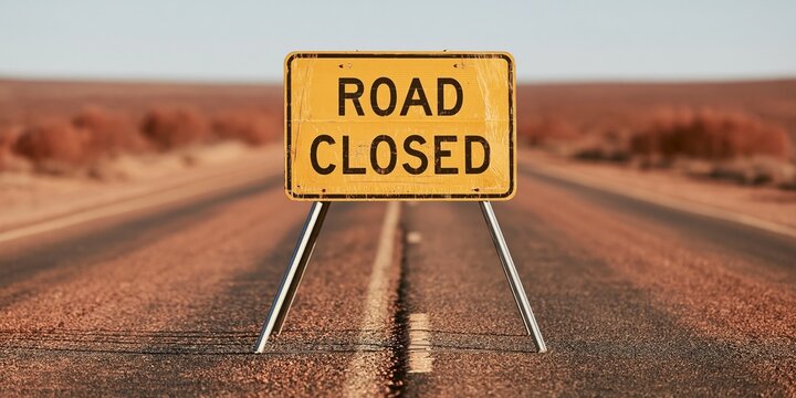 Road Closed Sign Standing on Empty Desert Highway Under Clear Sky