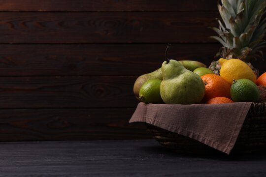 Different fresh fruits in wicker basket on black wooden table, closeup. Space for text
