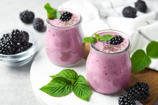 Tasty blackberry smoothies with chia seeds, berries and leaves on light grey table, closeup