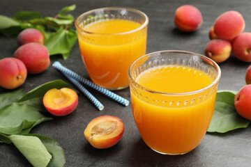 Apricot juice in glasses, fresh fruits and drinking straws on black table, closeup © New Africa
