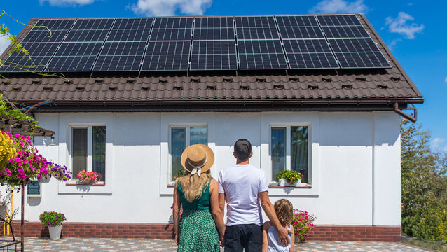A family looks at solar panels on the roof of a house. Selective focus.