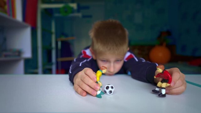 A young soccer fan plays with miniature football player figures in his bedroom, recreating the excitement of the sport through imaginative play. Childhood hobby, sports fandom, and indoor creativity.