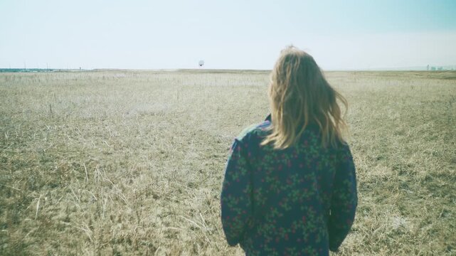 Woman walking away into vast open prairie with hair blowing in the wind
