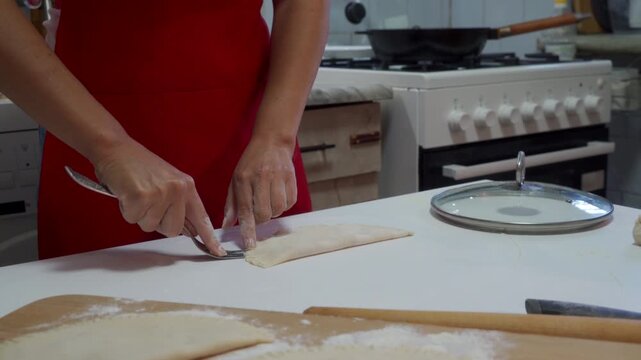 A focused cook carefully spreads savory meat filling onto a circle of raw dough using a fork. They work passionately at a white table in a bright kitchen during a neat homemade cooking routine.