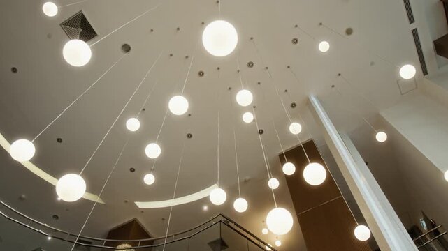 Modern spherical pendant lights hanging from high ceiling in luxury hotel lobby, camera rotating slowly in low angle shot. Footage ideal for hospitality marketing and interior design showcases