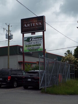 Gatineau, Quebec, Canada &ndash; June 28, 2026: A multi-business sign displays "Atelier Arteva" and "F. Auger" above parked cars and a chain-link fence on Bd Saint-Ren&eacute; E.