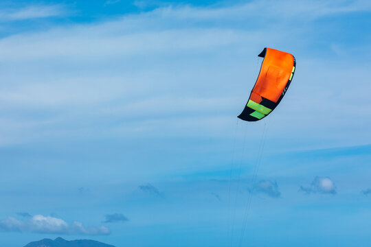 Colorful orange and green kite soaring against a bright blue sky with scattered clouds and distant mountains in the background. water sports concept. Copy space
