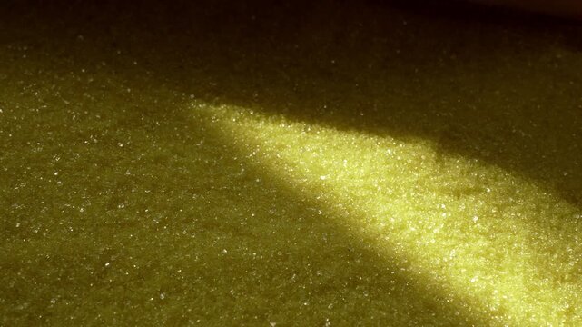 Close-up granular yellow crystals with moving diagonal sunlit highlight across uneven surface, with granule, crystal, yellow, texture detail, showing macro, closeup, surface, sparkle context