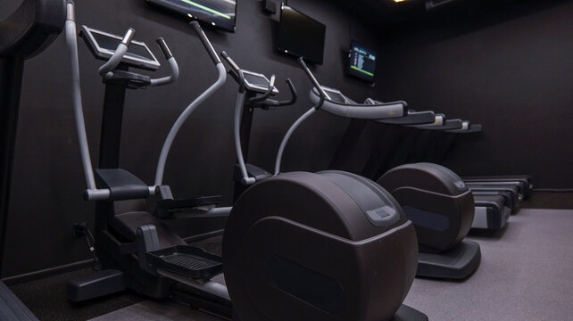 Modern gym equipment with treadmills and elliptical machines in a dark room