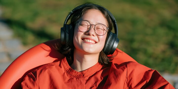 Teen wearing glasses and large headphones smiling with eyes closed outdoors for background and banner design in sunny park