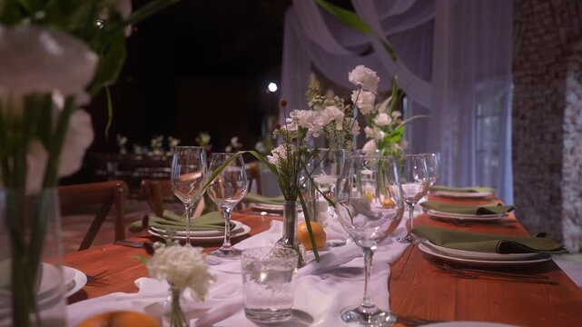 Elegant rustic banquet table with floral centerpieces and glassware set for reception, with table, centerpiece, wineglass, glass detail, showing vase, flower, floral, petal context
