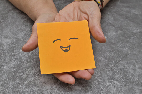 Hands holding an orange Post-it note with a drawn smiley face.