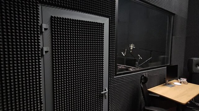 Soundproof studio with padded walls and glass window. Desk and chair inside the recording booth. Professional setup for audio or voice-over recording