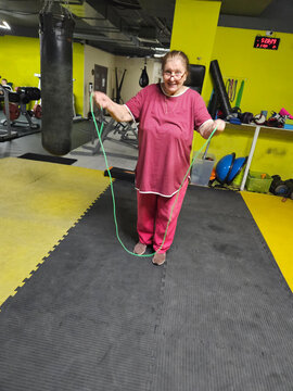 Woman jumps rope in vibrant gym setting. She wears pink athletic outfit. Yellow walls and padded floor surround her. She smiles, actively engaged in exercise. Black punching bag hangs nearby