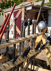 Naklejka premium Swords and knight armor displayed on wooden stand medieval historical event. Reenactment scene related to heritage, medieval culture, traditional skills and entertainment.