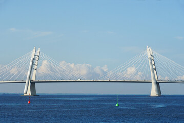 Fototapeta premium A modern cable-stayed automobile bridge spans the vast ocean under a clear blue sky.