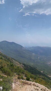High-angle panning shot of lush green mountain slopes and distant valley, filmed from moving cable car in Montenegro