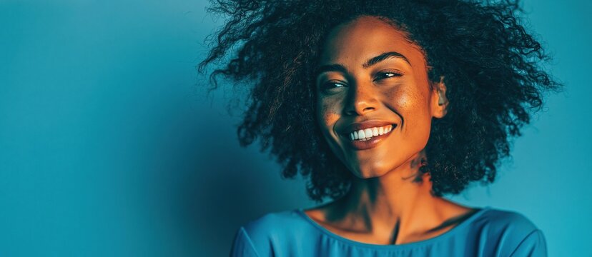 Smiling woman with voluminous natural curls wearing a teal top against a turquoise background with directional light Theme of joyful self expression