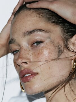 Close up profile portrait of a freckled woman with slicked back hair and loose strands across her face touching her head Theme of natural beauty