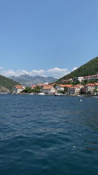 Coastal Lepetane village in Montenegro with red-roofed houses along the waterfront beneath green hills and distant mountains