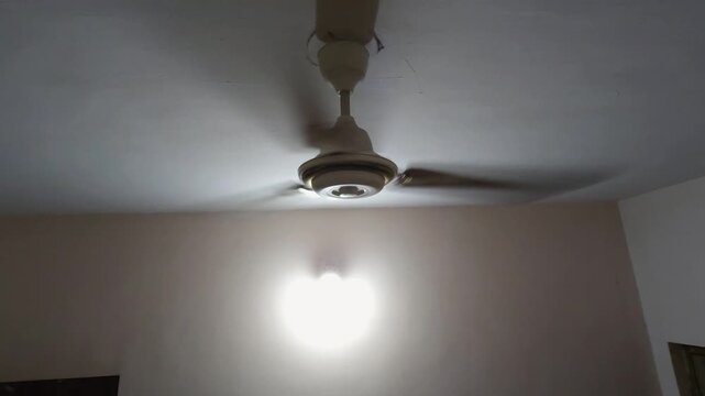 An old ceiling fan hums loudly against a cracked ceiling, illustrating the rising energy demands as households try to combat increasing global temperatures.