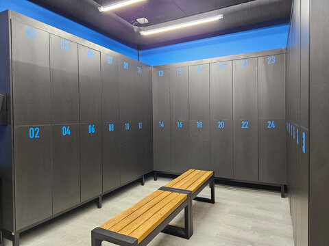 Modern locker room with blue-lit storage and wooden bench in middle with electronic lock