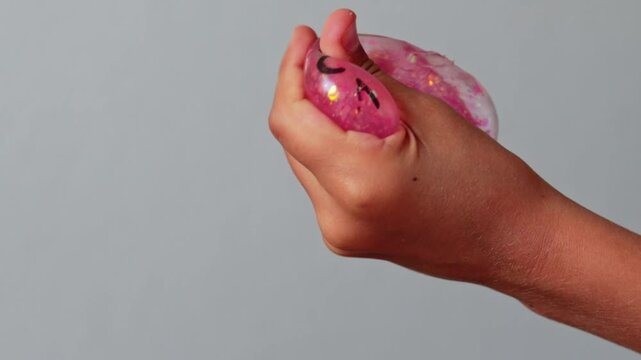 Child's hand squeezes a pink squishy dumpling toy, showcasing the deformation and return to shape in a playful indoor setting against a neutral background