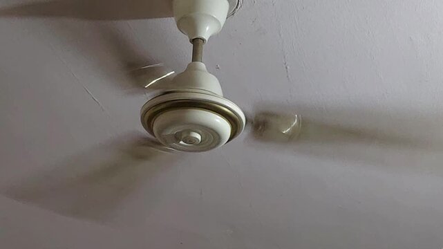 A close-up shows a fan's pull chain swaying violently at high speed, representing the strain on local power grids during a severe seasonal heat emergency.