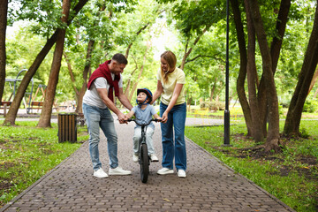 Fototapeta premium Happy parents teaching their son to ride bicycle in park. Child safety