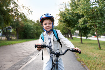 Naklejka premium Portrait of smiling boy in protective helmet on bicycle in park. Child safety