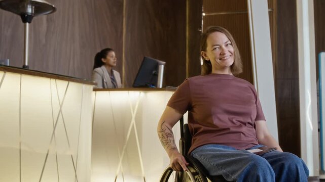 Portrait of young adult Caucasian woman with disability in wheelchair smiling at camera in hotel lobby. Video is ideal for promoting accessible travel and inclusive hospitality services