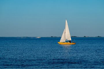 Fototapeta premium White sailboat crossing calm blue water beneath a clear sky