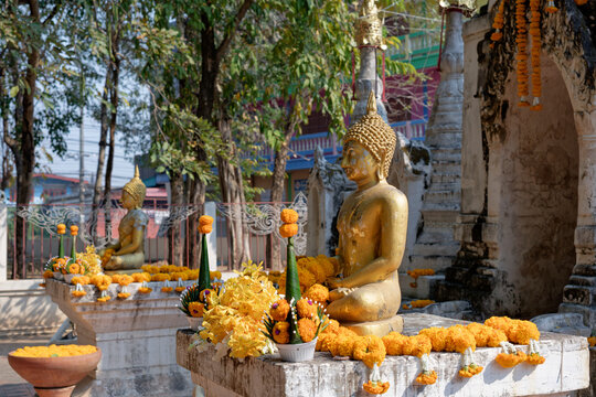 Golden Buddha statues with marigold flower garlands and traditional offerings at Wat Chom Sawan in Phrae, Thailand.