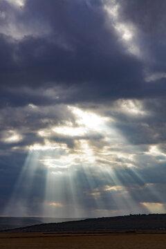 Dramatic sunbeams breaking through dark storm clouds over landscape
