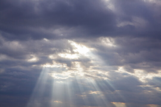 Sunbeams breaking through dramatic dark storm clouds in cloudy sky