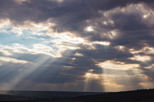 Dramatic sunbeams shining through storm clouds over rural landscape