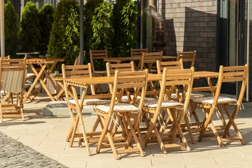 Fototapete Gastronomie Empty outdoor cafe terrace with wooden tables and chairs in sunlight  © Anastasiia