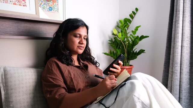 Woman asking AI assistant for help while writing notes at home, generative AI, research, brainstorming, productivity and digital workflow concept