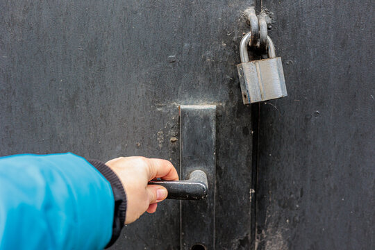 Hand Grasping Door Handle Next To Padlock On Metal Door Suggesting Access And Security