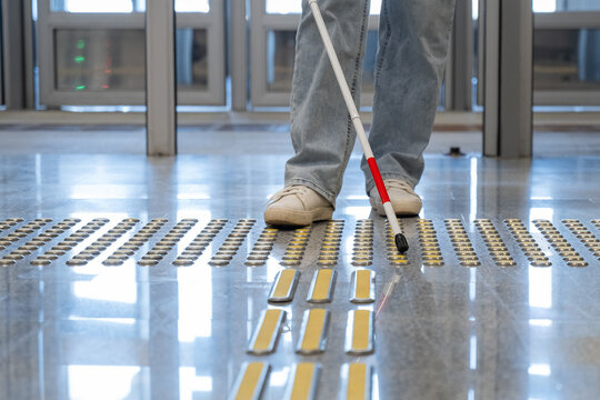A blind woman walks on tactile paving. Close-up of her feet and a walking stick.